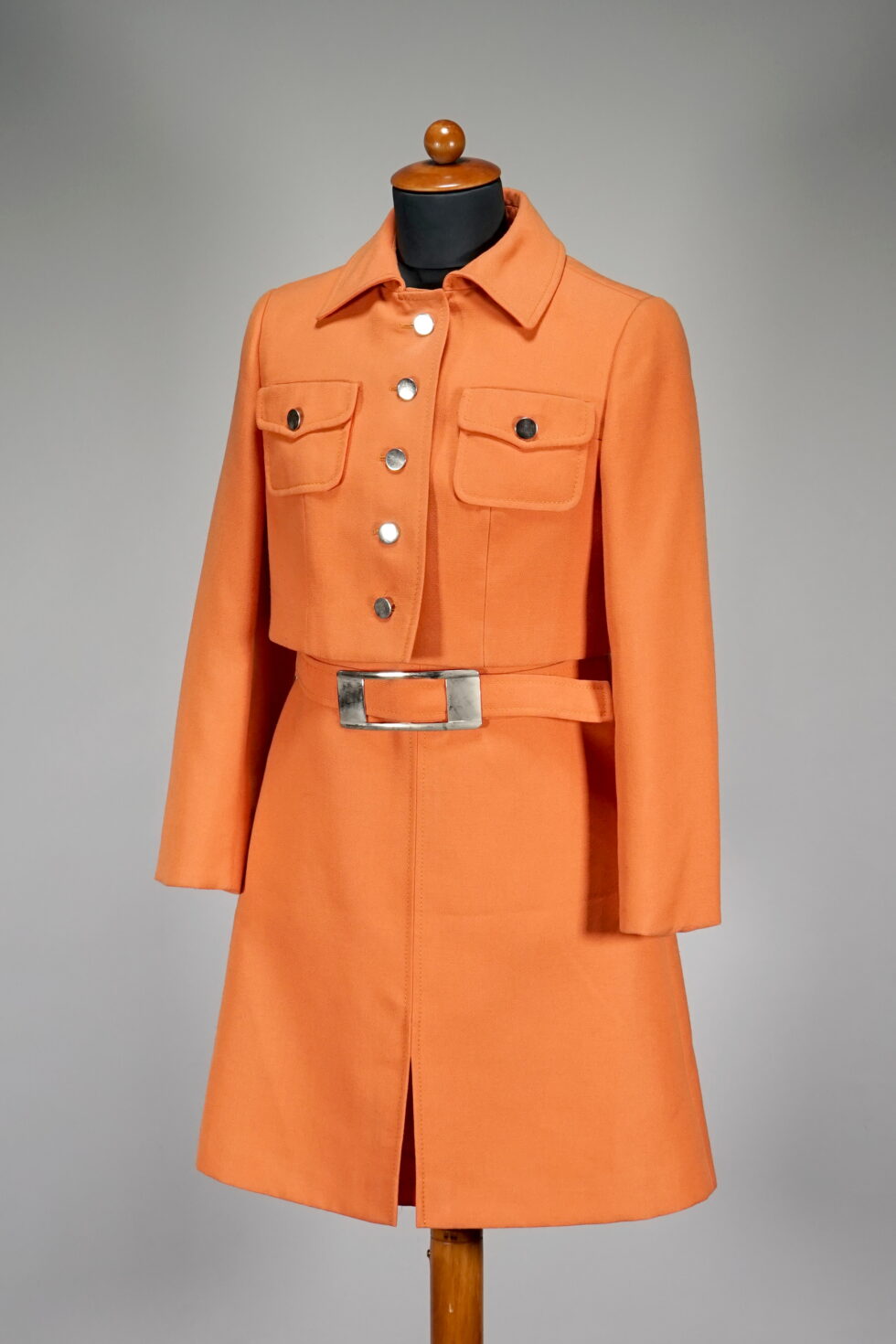 Kurze orangene Kostümjacke und ärmelloses Kleid mit breiter Gürtelschnalle